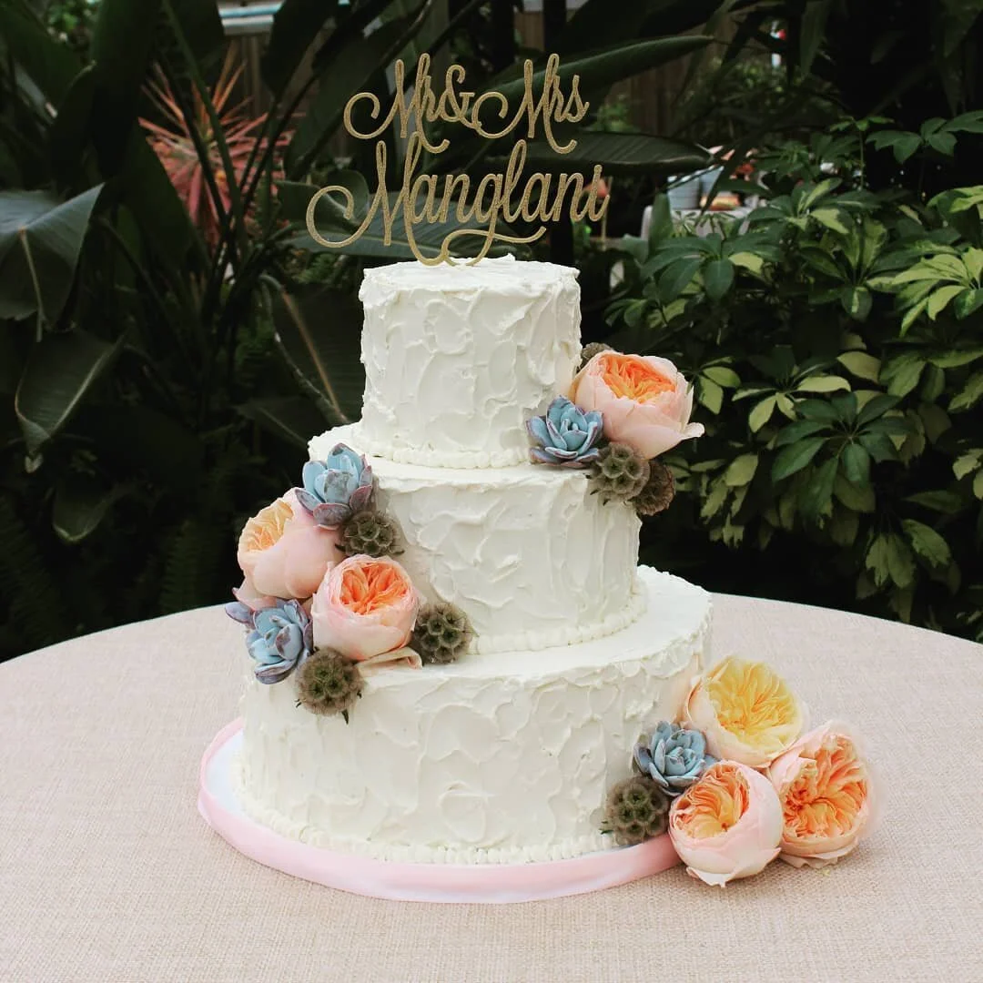 An outdoor tiered wedding cake adorned with fresh florals at an AMR Catering wedding.